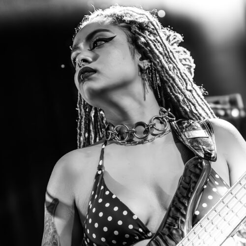 Musikerin mit Dreadlocks spielt Bass, ernst, gepunktetes Outfit, schwarz-weiße Fotografie.